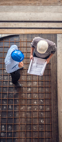 Top-down view of two construction workers looking over blueprints.