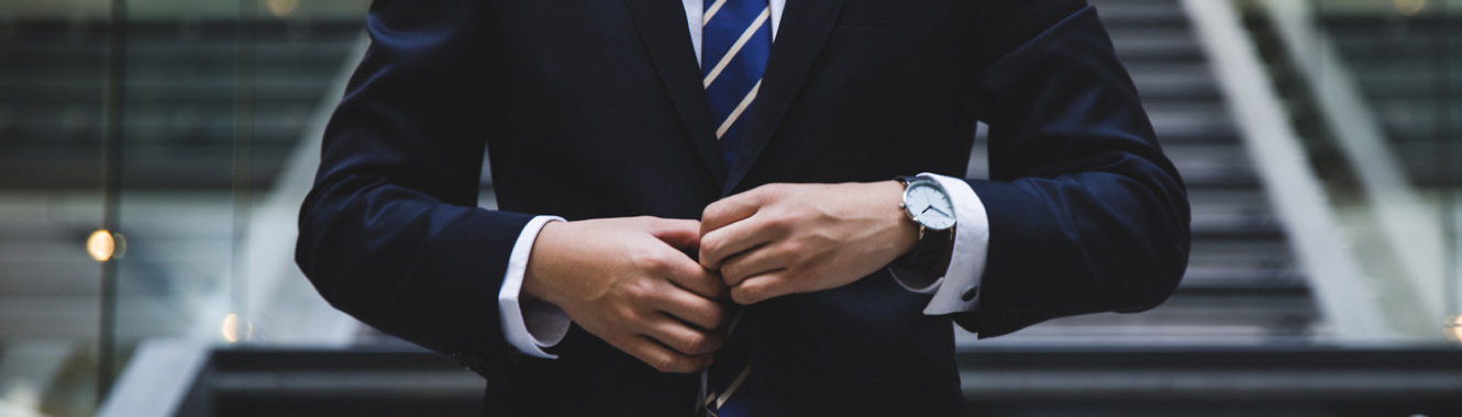 Close-up shot of a man hand's buttoning up his expensive-looking business suit. He's standing in a modern office building.