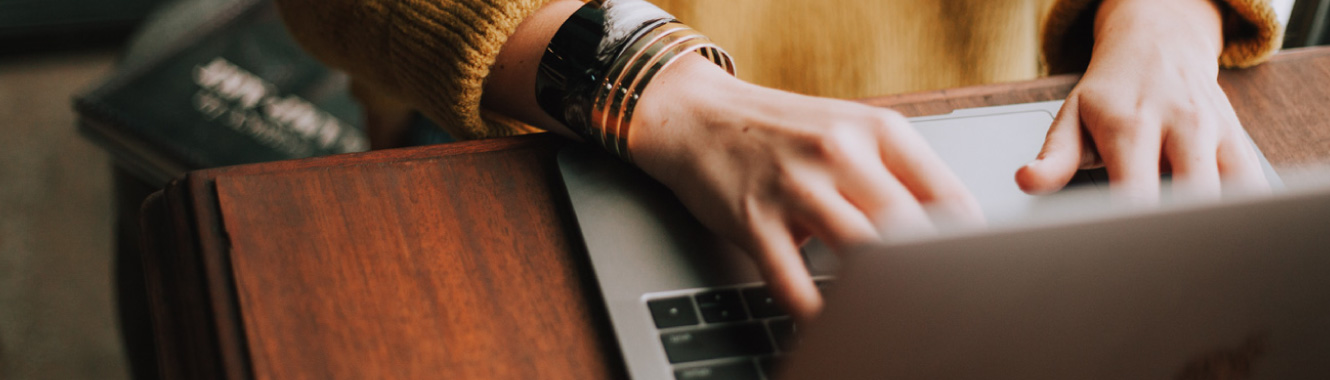 A close-up of a young woman's hands typing on a modern laptop.