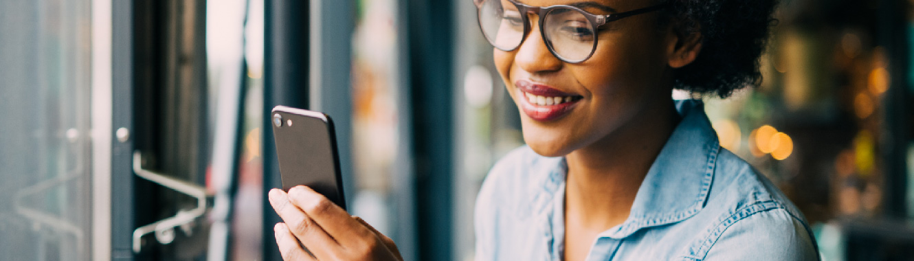 A young woman in a trendy restaurant looking at her smartphone and smiling.